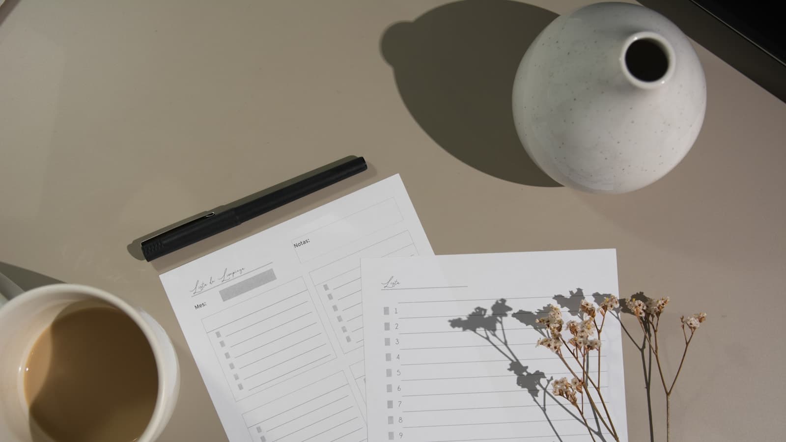 Two blank printed checklists and a pen on a warm neutral desk, beside a mug of coffee and dried botanicals casting a soft shadow across the page.
