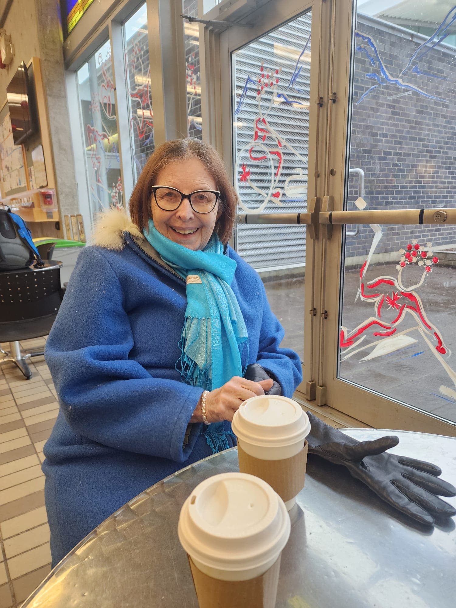 The senior in Samantha's life sitting at a community-centre table over coffee, smiling.